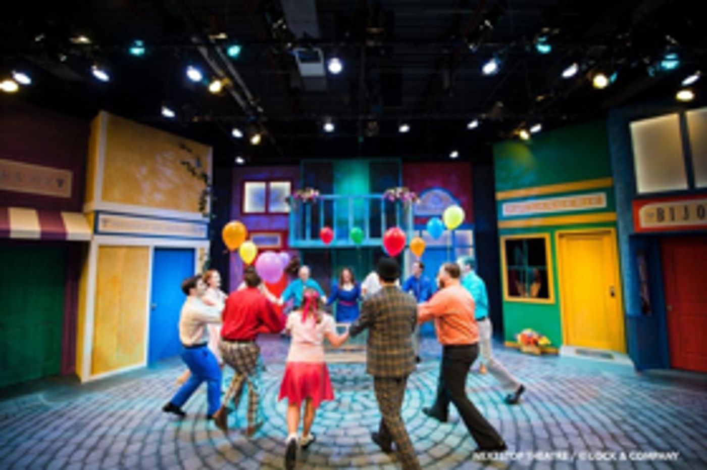 The cast of Amour dances with balloons in their hands in the town square.