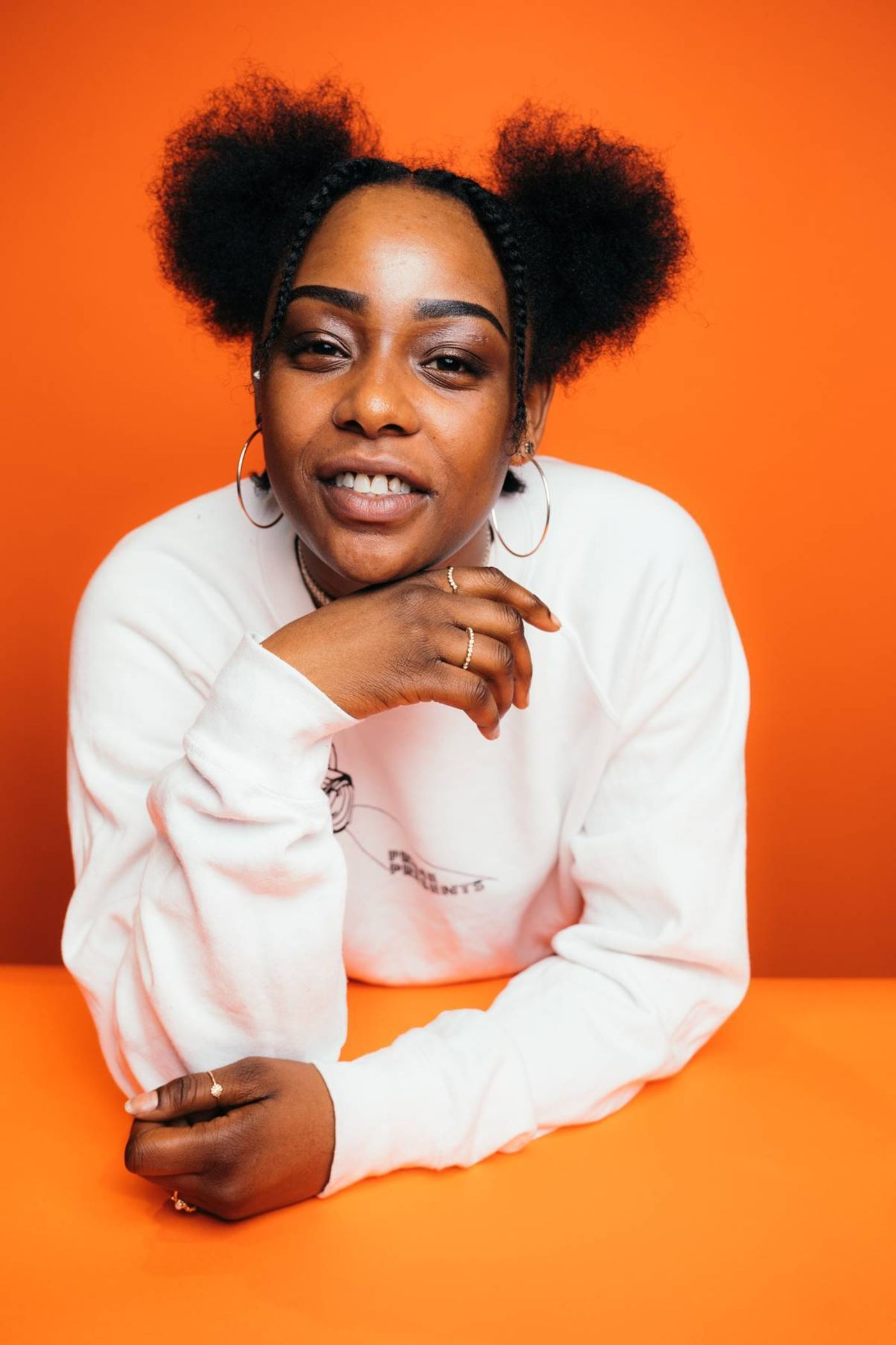 Photo of Basheba Baptiste leaning forward on an orange surface