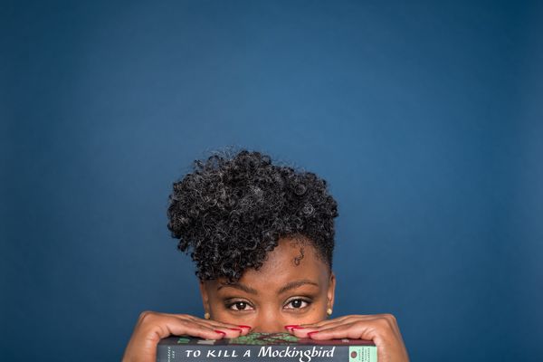 A young woman peeking up at us, holding a copy of To Kill a Mockingbird 1