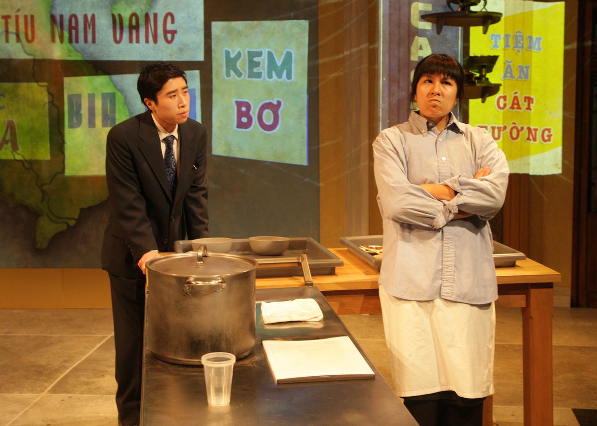 Dustin Vuong Nguyen as Quang and Hannah Mariah as Mùi in the rolling world premiere of "Colonialism is Terrible, But Phở is Delicious," playing March 31 - April 30, 2023 at Better Aitken theater arts Center on the Cripe Stage. Written by Dustin H. Chinn; Directed by Oánh Nguyễn. Photo by Doug Catiller, True Image Studio. 