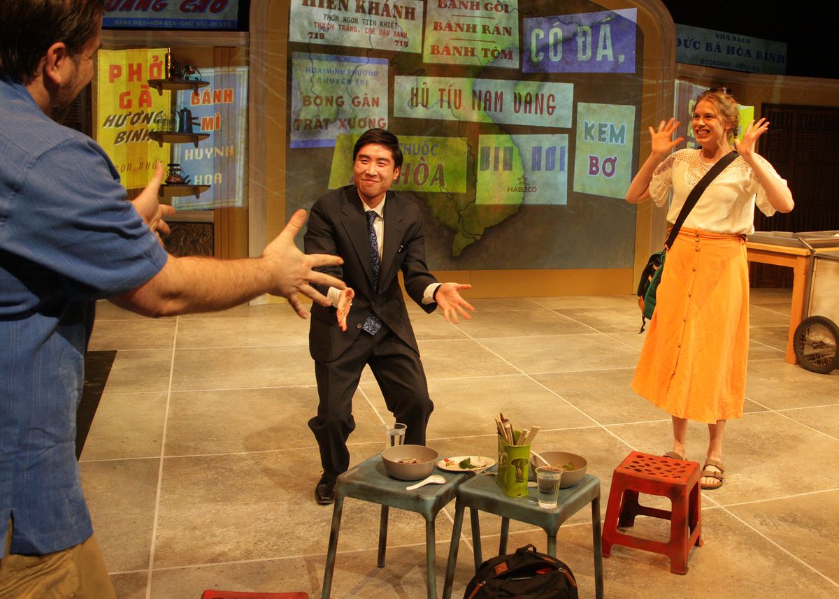 Casey Long as Hugh, Dustin Vuong Nguyen as Quang, and Chloe Gay Brewer as Rose in the rolling world premiere of "Colonialism is Terrible, But Phở is Delicious," playing March 31 - April 30, 2023 at Better Aitken theater arts Center on the Cripe Stage. Written by Dustin H. Chinn; Directed by Oánh Nguyễn. Photo by Doug Catiller, True Image Studio. 