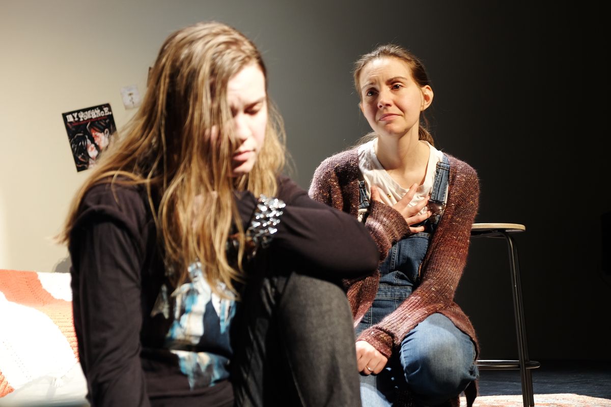 Teen Mak, played by actor Elizabeth Eby (left) looks down, distraught as Adult Mak, played by playwright and actor Makayla Baker Paxton (right) looks longingly at her with her hand on her heart.