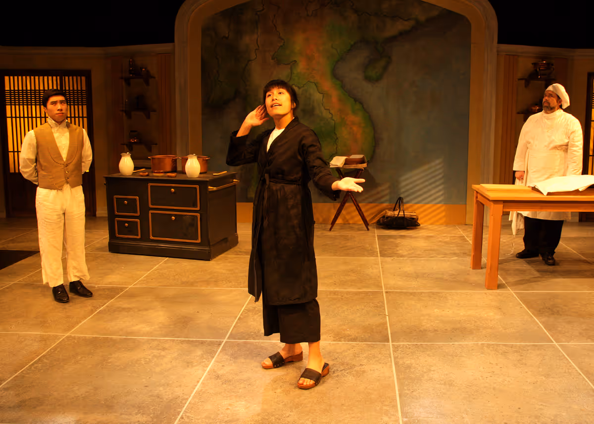 Dustin Vuong Nguyen as Nguyễn, Hannah Mariah as Thúy, and Casey Long as Guillaume in the rolling world premiere of "Colonialism is Terrible, But Phở is Delicious," playing March 31 - April 30, 2023 at Bette Aitken theater arts Center on the Cripe Stage. Written by Dustin H. Chinn; Directed by Oánh Nguyễn. Photo by Doug Catiller, True Image Studio.