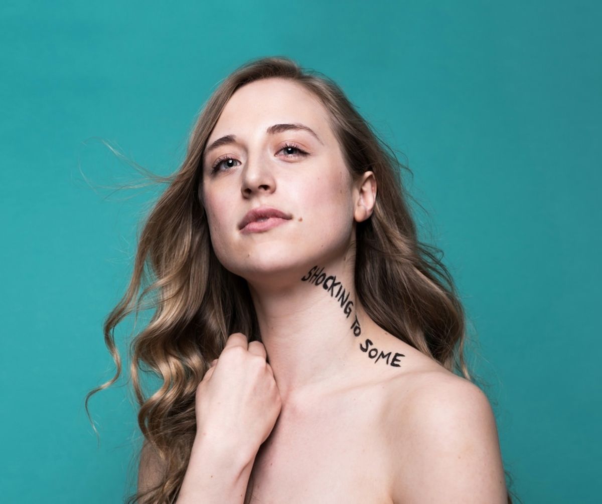 A young woman, bare shoulders, with the words "Shocking to Some" written across her neck and collar bone