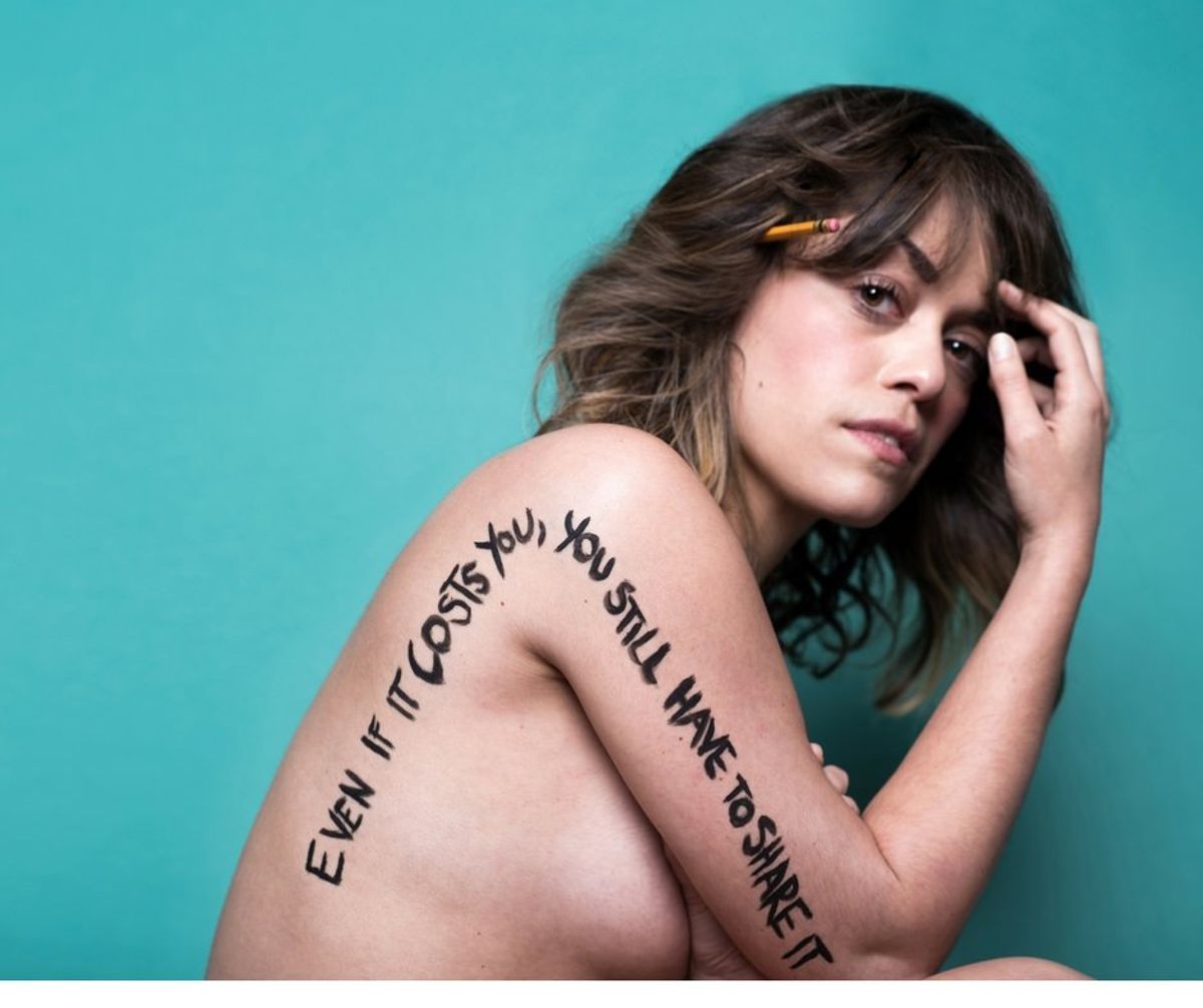 young woman, bare shoulders, with the words "Even if it costs you, you still have to share it" written along her arm and shoulder