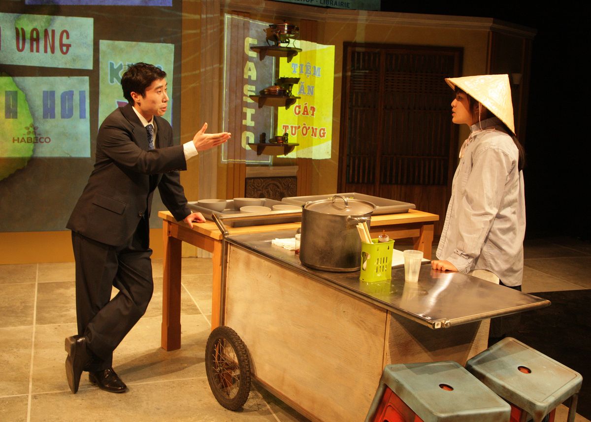 Dustin Vuong Nguyen as Quang and Hannah Mariah as Mùi in the rolling world premiere of "Colonialism is Terrible, But Phở is Delicious," playing March 31 - April 30, 2023 at Better Aitken theater arts Center on the Cripe Stage. Written by Dustin H. Chinn; Directed by Oánh Nguyễn. Photo by Doug Catiller, True Image Studio. 