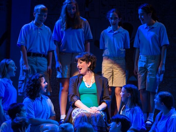 The Narrator, played by Laura Berger, surrounded by members of the children''s chorus Photo
