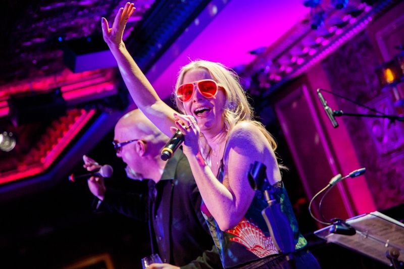 Jessica Hendy sings into a hand held microphone and her right hand raised.