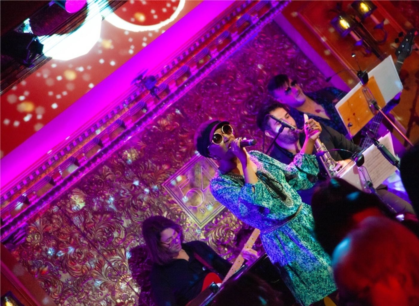 Jessica Briago sings into a handheld mic in front of a small band.