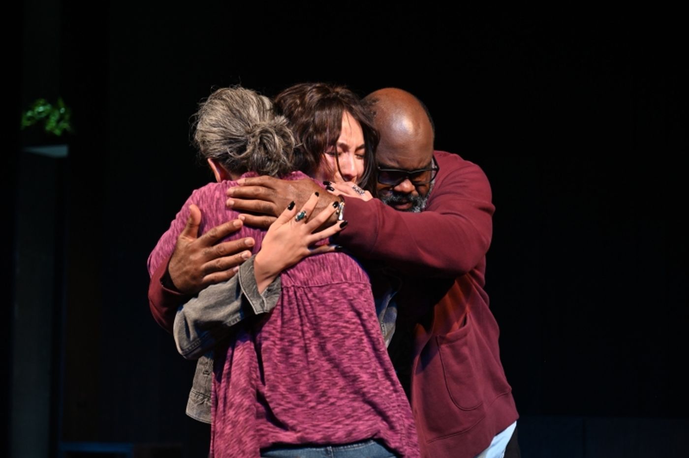 Three people embrace in a group hug, from left to right a woman, a teenager, and a man