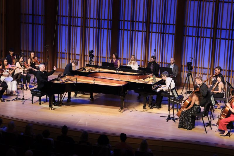Three pianos on stage amidst other musicians